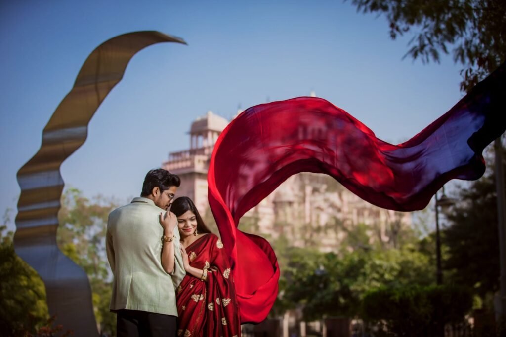 A romantic couple embraces outdoors with a vibrant red scarf billowing in the wind.